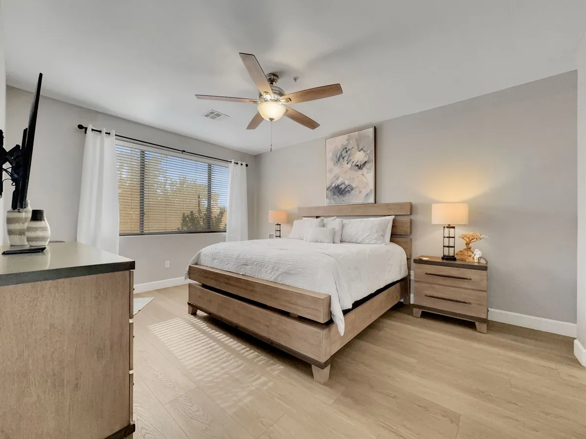 A peaceful bedroom scene showing a comfortable bed, nightstands, artwork, and a window letting in gentle sunlight. The space feels inviting and perfect for relaxing or unwinding at the end of the day.