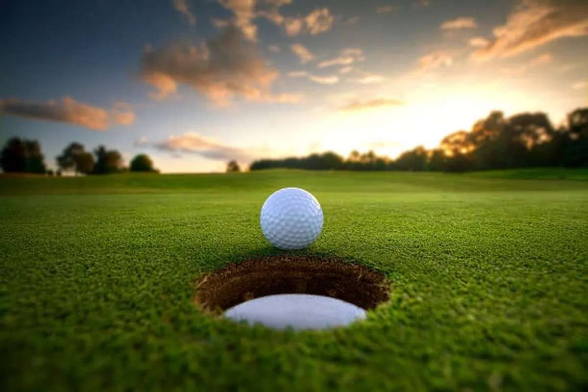 This image features a golf ball resting near the hole on a meticulously maintained green, set against a backdrop of lush grass and a tranquil outdoor setting. The peaceful atmosphere underscores the leisure and enjoyment associated with golfing at premier courses.