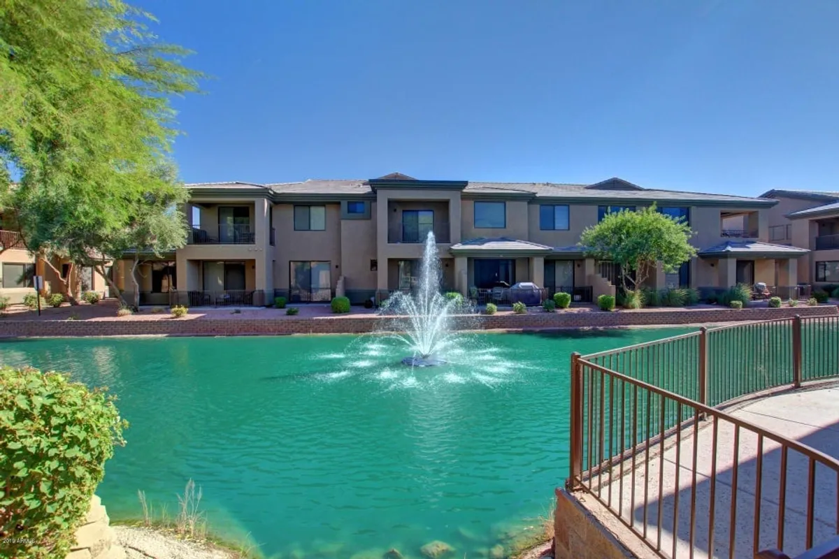 This exterior shot features a peaceful pond with a flowing fountain surrounded by lush greenery and the balconies of the apartment buildings overlooking the water. Residents can be seen relaxing by the pond or enjoying the balcony views, all set within a tranquil, resort-inspired landscape.