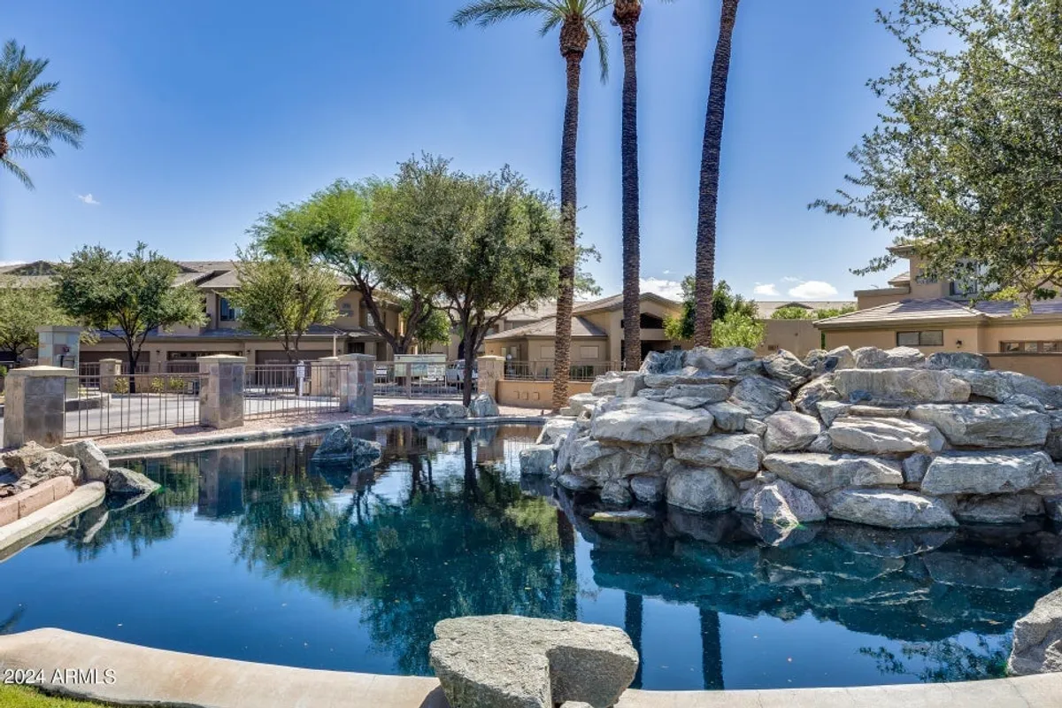 A serene swimming pool surrounded by natural rock formations, lush palm trees, and greenery. The calm water and well-landscaped environment create an oasis-like setting perfect for outdoor relaxation, whether it's a morning coffee or a leisurely afternoon by the pool.