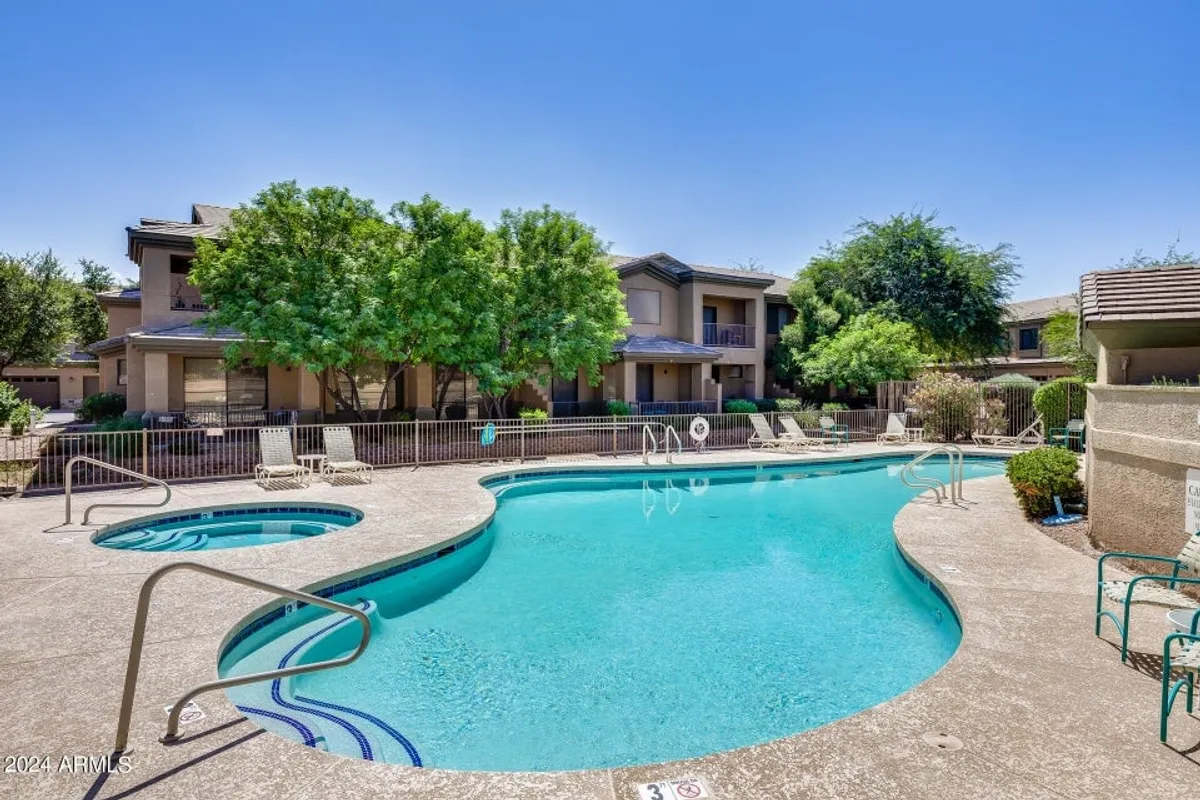 A sunlit swimming pool surrounded by greenery, lounge chairs for relaxation, and a nearby hot tub create a leisurely and inviting community centerpiece. The scene suggests activities like swimming, sunbathing, and socializing.