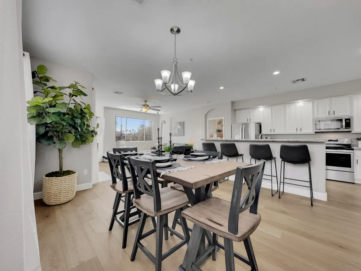 A warm and inviting dining area is set for a meal, with a chandelier overhead and a spacious kitchen counter in view. The table is ready for gatherings, suggesting opportunities for guests to share meals and stories in a home-away-from-home setting.