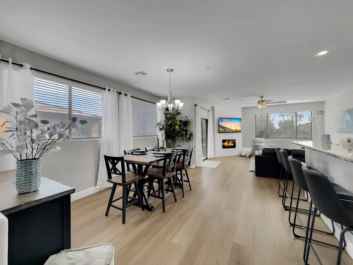 This image shows an open-concept interior featuring a dining table, television, fireplace, and a kitchen island. The space is arranged to facilitate both dining and lounging, with the fireplace and TV serving as focal points that enhance the cozy, social ambiance. Warm lighting and tasteful decor make the area feel welcoming and ready for gatherings or relaxing evenings.